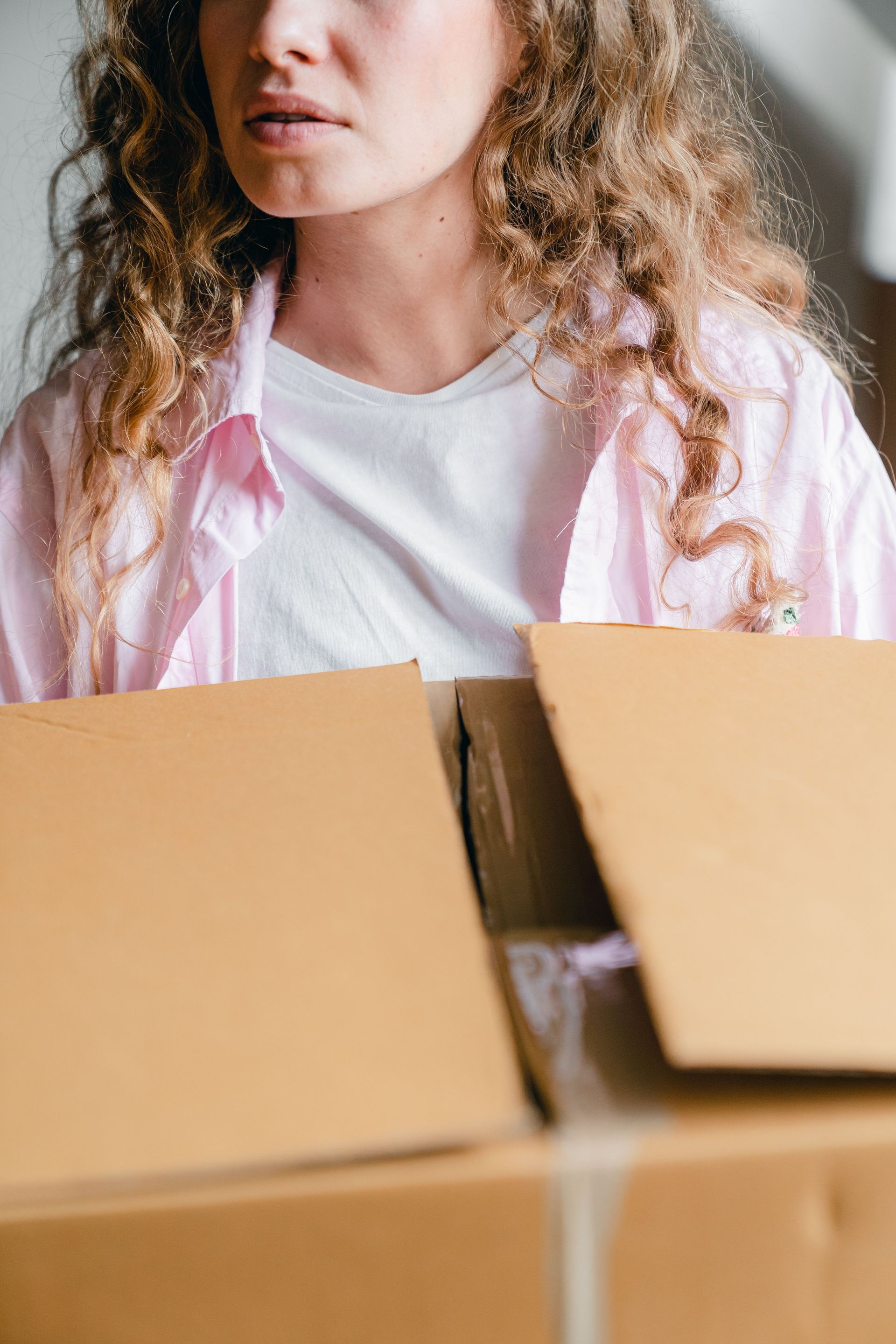 Crop young female in casual clothes holding carton box while moving into new contemporary apartment